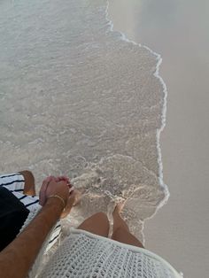 two people are sitting on the beach with their feet in the water and holding hands