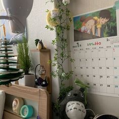 a desk with a calendar on the wall next to plants and other things in front of it