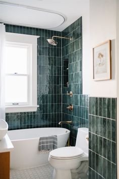 a white toilet sitting next to a bath tub in a bathroom with green tile on the walls