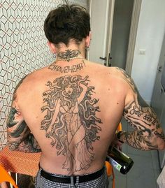 a man with tattoos on his back holding a wine bottle