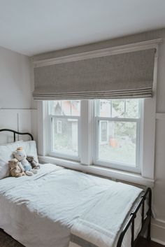 a white bed sitting under two windows in a bedroom