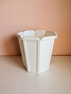 a white vase sitting on top of a table next to a pink wall and floor