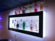 an illuminated shelf with bottles and glasses on it in front of a wall mounted mirror