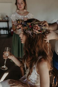 the bride is getting ready to put her hair down with flowers on her head and holding a wine glass in her hand