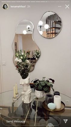 two mirrors on the wall above a table with vases and flowers in front of it