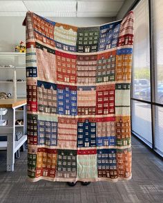 a large multicolored quilt hanging from the ceiling in an office area with windows