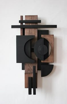 a wooden sculpture with black and brown shapes on it's face, against a white wall