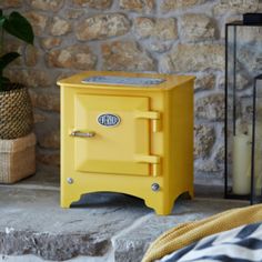 a yellow stove sitting on top of a stone floor next to a potted plant