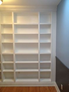 an empty room with white bookcases on the wall and wood flooring in front of it