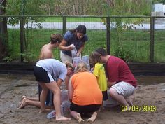 several people are gathered around a box on the ground in front of a fenced area