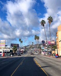 a street lined with palm trees under a blue sky filled with fluffy white puffy clouds