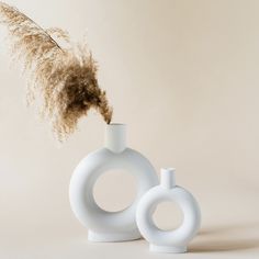 two white vases sitting next to each other with dry grass sticking out of them