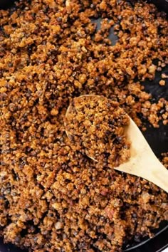 a wooden spoon is in a black pan filled with granola crumbled on top