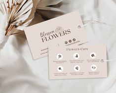 two business cards sitting on top of a bed next to some dried flower buds and flowers