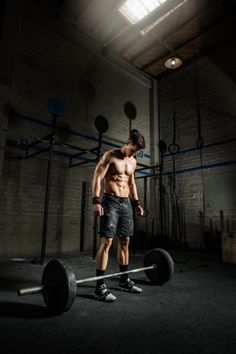 a shirtless man holding a barbell in a dark gym area with no shirt on