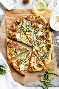 a sliced pizza on top of a wooden cutting board next to green beans and asparagus