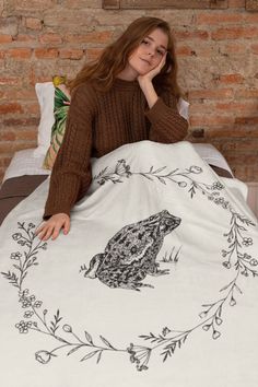 a woman sitting on top of a bed covered in a white and black frog blanket