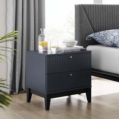 a bed with a gray headboard and blue pillows on it next to a night stand