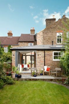 an outdoor patio with chairs and tables in front of a brick house on a sunny day