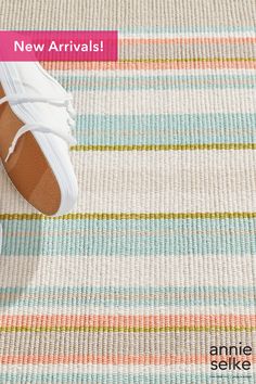 a pair of white tennis shoes sitting on top of a striped rug with the words new arrivals