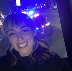 a woman is smiling while sitting in a car at night time with the city lights behind her