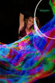 a woman is doing tricks on a hula hoop with colorful lights in the background