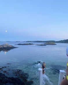 two people are standing on a boat in the water and looking out at an island