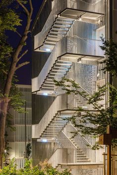 a tall building with many stairs lit up at night in front of trees and bushes