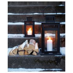 two lit candles sitting on top of steps next to firewood and logs in the snow