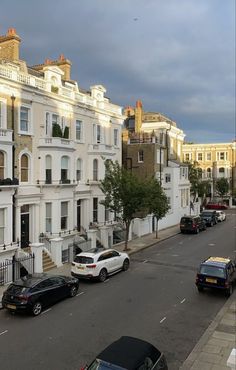 several cars parked on the side of a street in front of white buildings with balconies