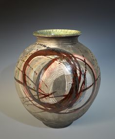 an artistic vase with red and green designs on the outside, in front of a gray background