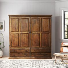 a large wooden armoire sitting in a living room next to a chair and potted plant