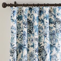 a blue and white floral curtain hanging from a metal rod, with the curtains pulled back