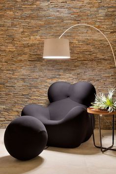 a modern living room with black chairs and a lamp on the side table in front of a stone wall