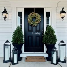 a black front door with two potted plants and three lanterns