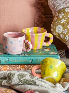 two coffee mugs sitting on top of a stack of books next to a pink chair