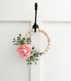 a pink flower is hanging from a door handle on a wooden beaded wreath with greenery