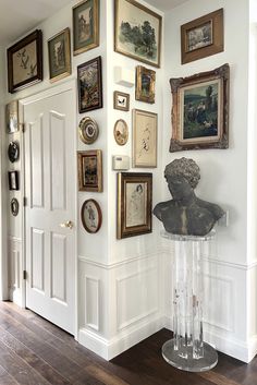 a room with many framed pictures on the wall and a busturine in the corner