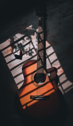 an acoustic guitar is sitting on the floor in front of a window with sunlight streaming through it