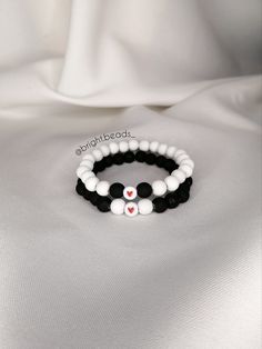 two bracelets with black and white beads are sitting on a white cloth covered surface