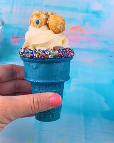 a hand holding an ice cream cone with sprinkles and two doughnuts on top