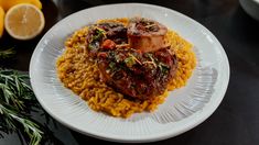 a white plate topped with meat and rice next to sliced lemons on a table