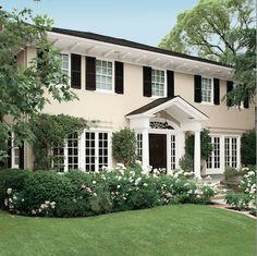 a white house with black shutters on the front and side windows is surrounded by lush greenery