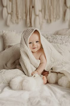 a smiling baby wrapped in a blanket on top of a bed with white fluffy balls