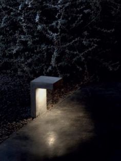 a concrete bench sitting in the middle of a park at night with lights on it