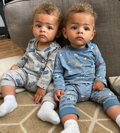 two toddlers sitting on the floor with their legs crossed and looking at the camera