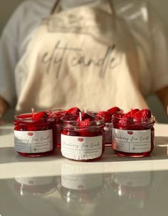 four jars of candles sit on a counter with a person in the background behind them