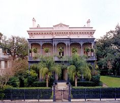 an old house with palm trees in front of it and a fence around the yard