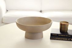 a table with a book and a bowl on it next to a white couch in a living room