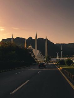 cars driving down the road in front of some tall buildings with spires on them